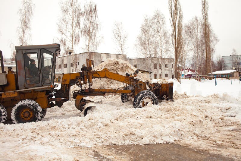 Clearing snow in Russia. Grader clears the way after a heavy snowfall. Tractor clears the road in the courtyard of a multi-storey. Building from snow. Excavator stock photography