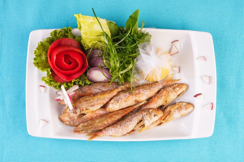 Fried fish in deep fat, capelin in batter with greens, tomatoes, cheese and red onion. European cuisine, Mediterranean dish. Fried fish in deep fat, capelin in royalty free stock photo