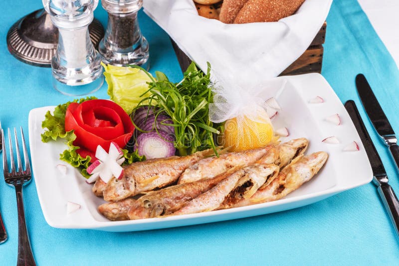 Fried fish in deep fat, capelin in batter with greens, tomatoes, cheese and red onion. European cuisine, Mediterranean dish. Fried fish in deep fat, capelin in stock photography