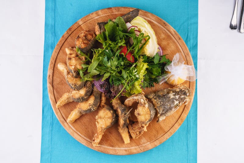 Fried fish in batter served with sliced ​​onion rings, greens, dill, pears, cilantro and dried squid straws. Mediterranean dish, European cuisine. Fried fish stock image