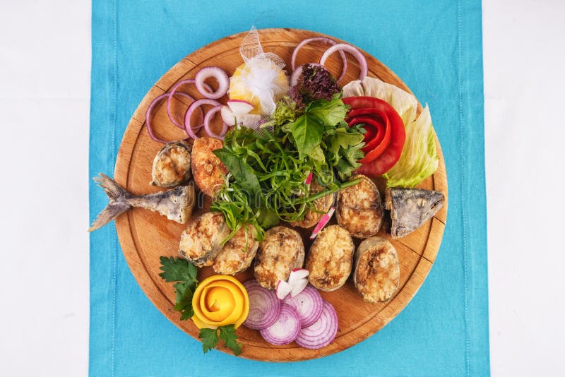 Fried fish in batter served with sliced ​​onion rings, greens, dill, pears, cilantro and dried squid straws. Mediterranean dish, European cuisine. Fried fish royalty free stock image