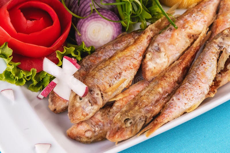 Fried fish in deep fat, capelin in batter with greens, tomatoes, cheese and red onion. European cuisine, Mediterranean dish. Fried fish in deep fat, capelin in royalty free stock image