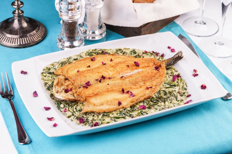 Fried steak of sea fish in batter, in a creamy sauce with greens and rose petals. Caucasian cuisine, Mediterranean food royalty free stock images
