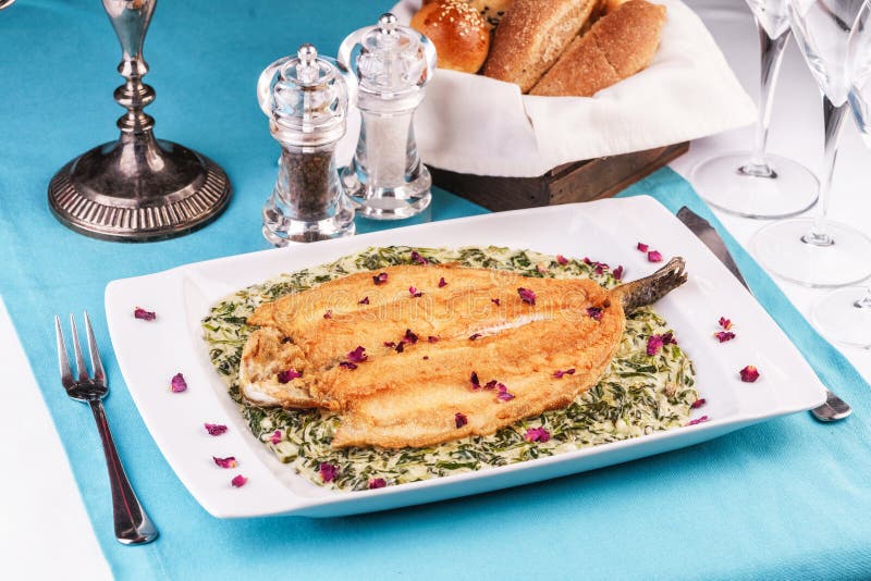 Fried steak of sea fish in batter, in a creamy sauce with greens and rose petals. Caucasian cuisine, Mediterranean food stock photography