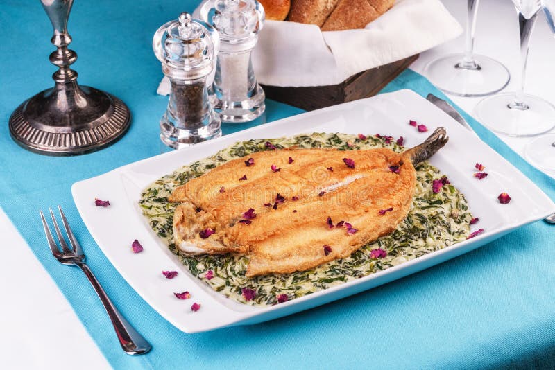 Fried steak of sea fish in batter, in a creamy sauce with greens and rose petals. Caucasian cuisine, Mediterranean food royalty free stock photo