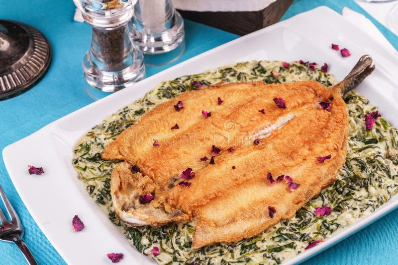 Fried steak of sea fish in batter, in a creamy sauce with greens and rose petals. Caucasian cuisine, Mediterranean food royalty free stock photography