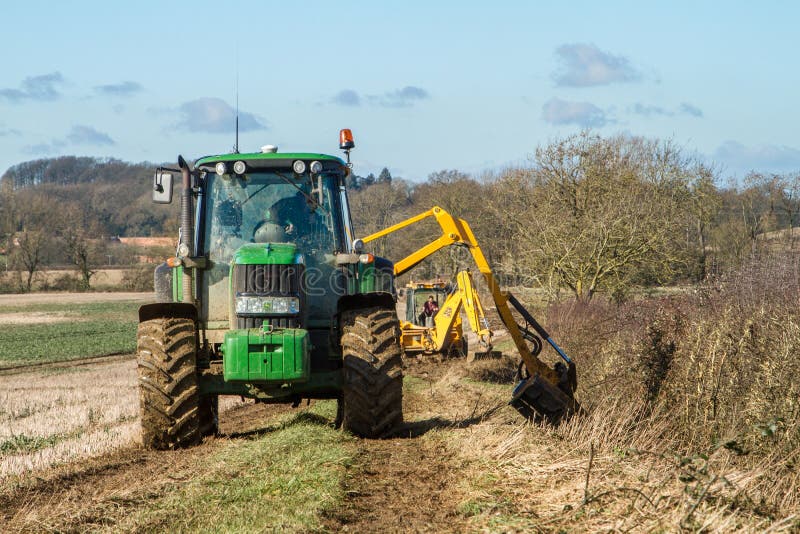 Green tractor hedge cutting and digger clearing a ditch. Green modern John Deere tractor cutting trimming hedge and jcb digger clearing out a ditch royalty free stock photography