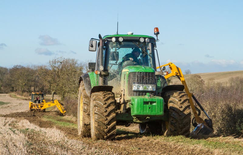 Green tractor hedge cutting and digger clearing a ditch. Green modern John Deere tractor cutting trimming hedge and jcb digger clearing out a ditch royalty free stock photography