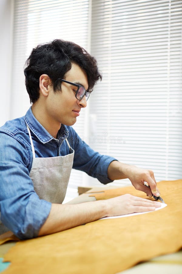 Cutting leather. Handcraft master cutting out small piece of beige leather from bigger one stock photography