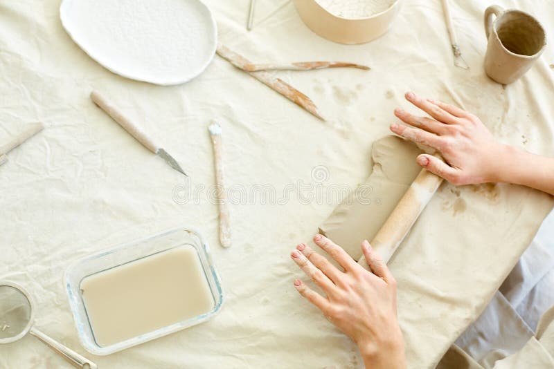 Rolling clay. Handcraft master making piece of white clay flat with help of wooden rolling-pin on table stock photo