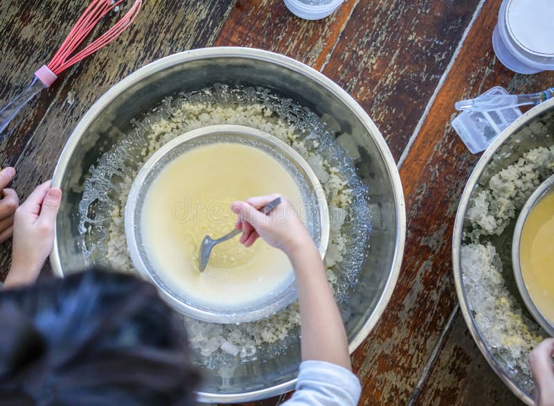 Kids` hand stirring homemade ice-cream mixture in crushed ice bowl stock image