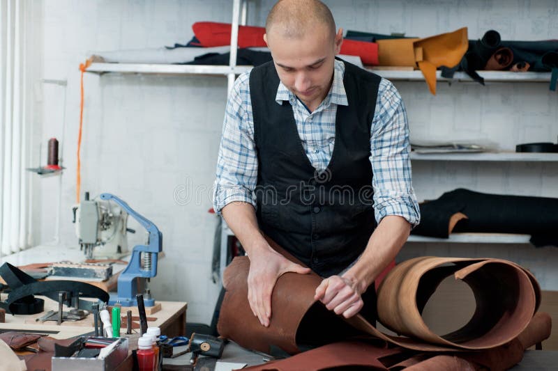 A master in the workshop, carefully examining the leather rolls. A master-artisan in the workshop, carefully examining the skin rolls stock photos