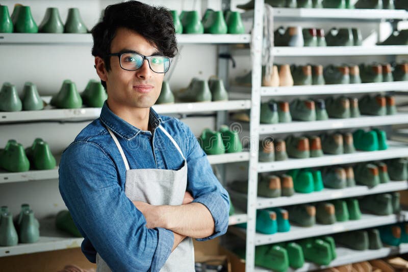 Master in workshop. Young cross-armed shoe master in uniform looking at camera royalty free stock photo