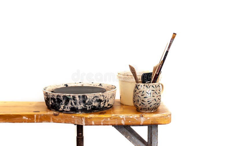 Tools for pottery with potters wheel are standing on the wooden table in messy studio, white isolated royalty free stock images