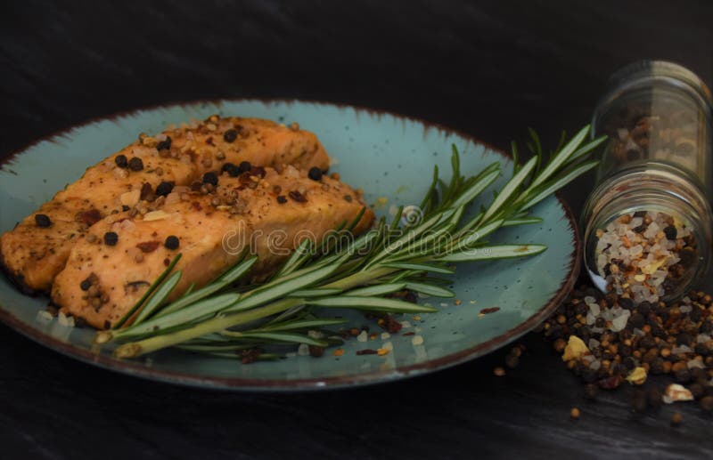 Two pieces of sturgeon fried fish. With a sprig of rosemary on a round plate and sprinkled with seasonings in a glass jar on a black background stock photo