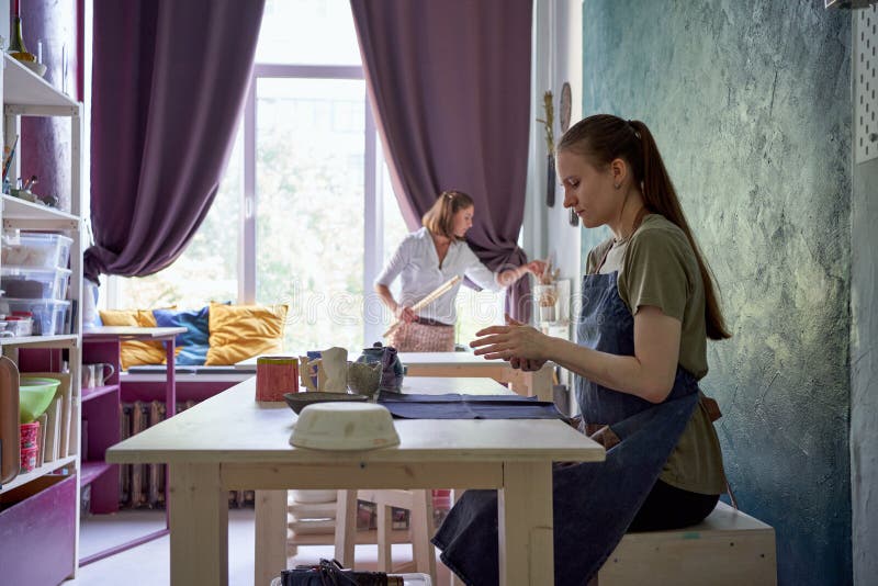 Master-class on making of utensils of clay, one female teaches another. Woman making ceramic pot on workshop. Concept for women in freelance, business. Handcraft stock photography