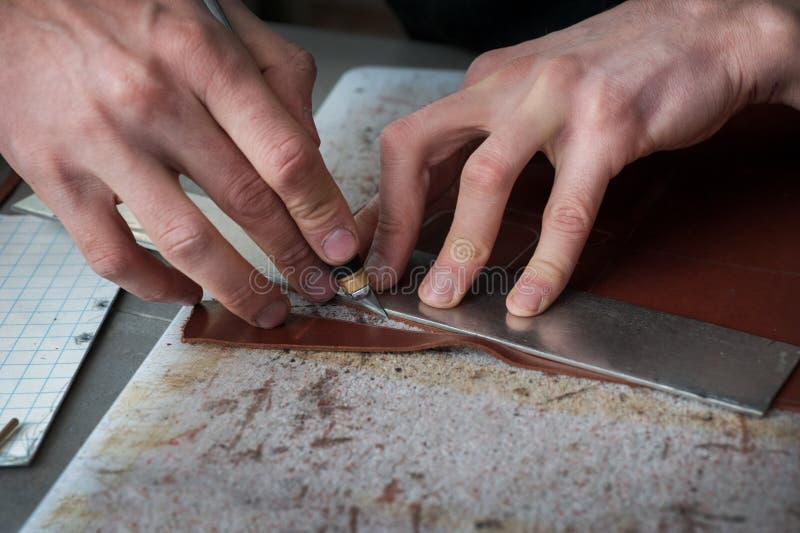 Hands of master cutting with a knife pattern from genuine leather closeup. Young male master working on cutting with patterns making leather goods. Hand-made stock photography